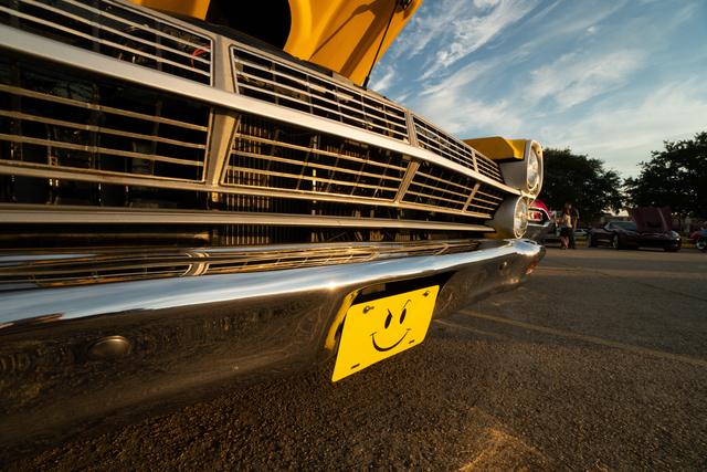 Close low-angle shot of a yellow Ford Fairlane's chrome grille and smiley-face license plate at golden hour