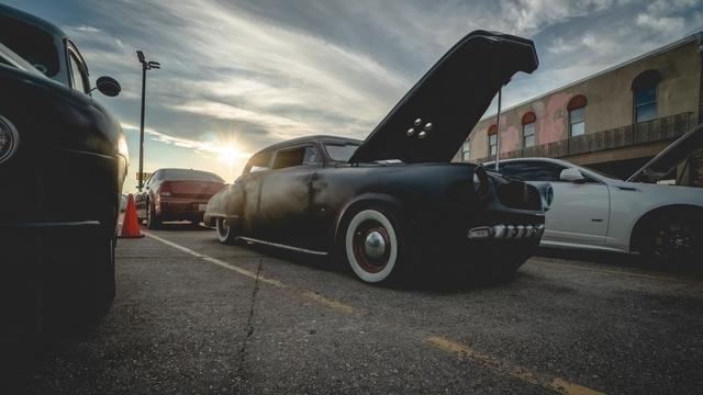 Matte black rat rod with open hood silhouetted at dusk